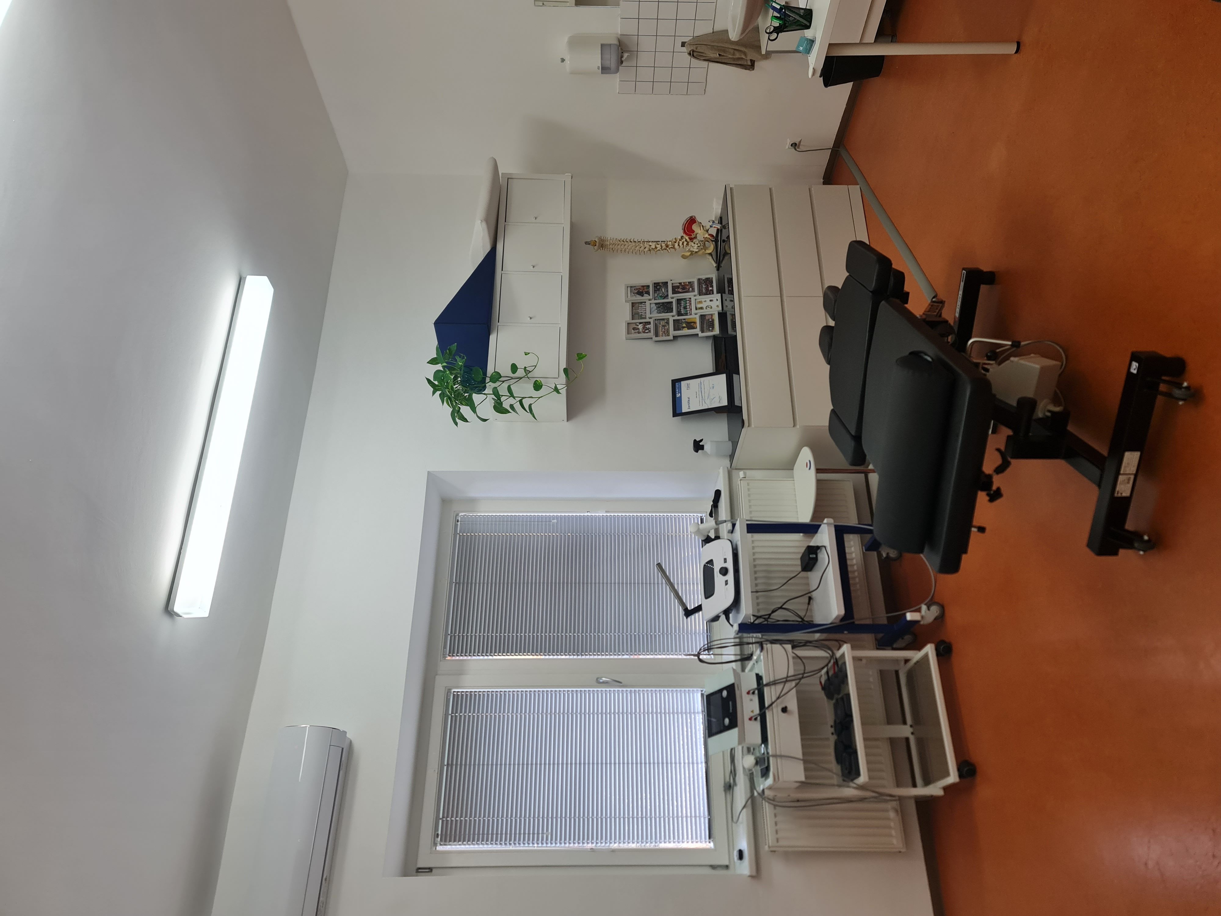Medical examination room with an adjustable black chair and various medical equipment.