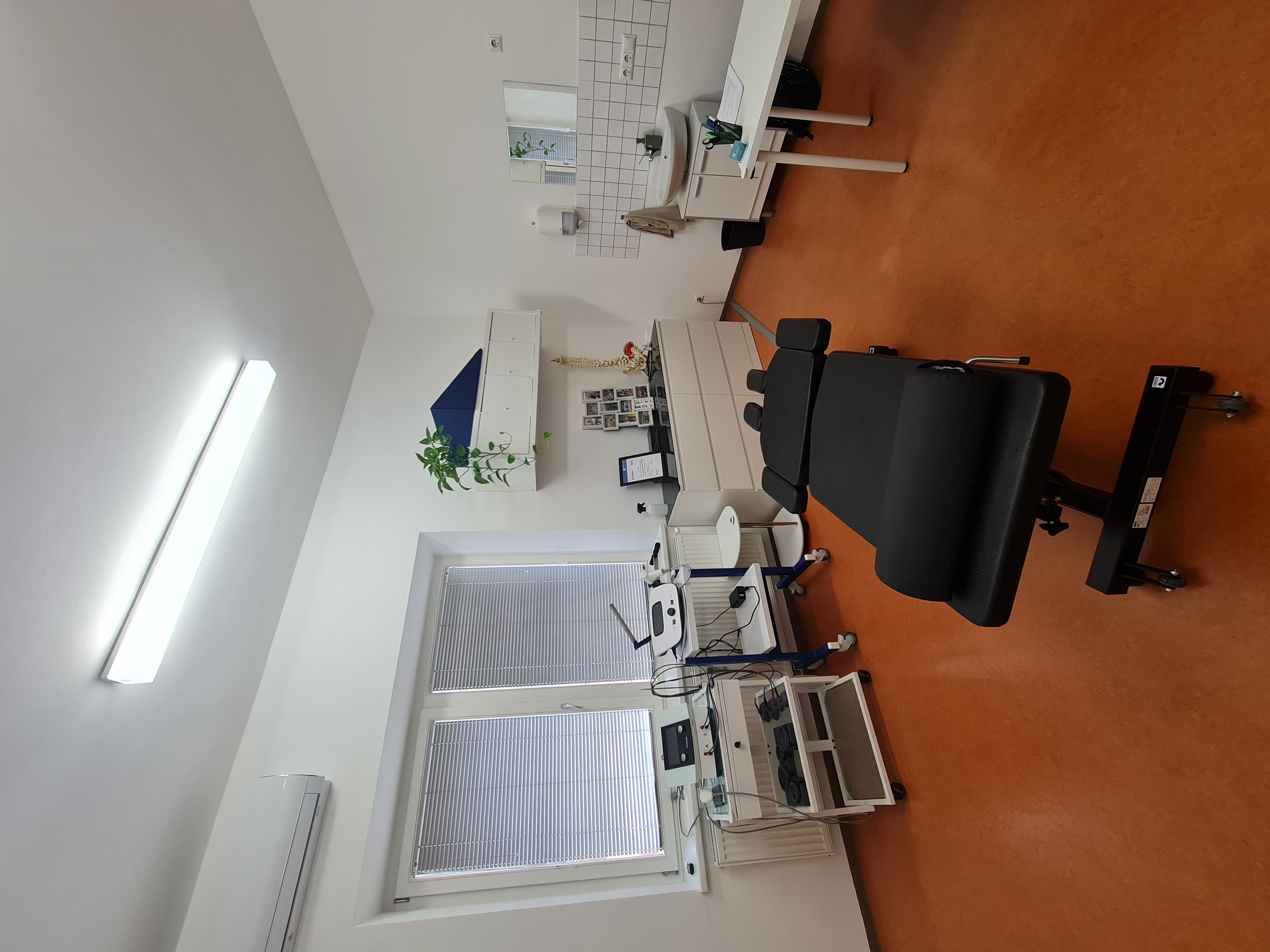 An ophthalmology examination room with a black chair, diagnostic equipment, and a window.