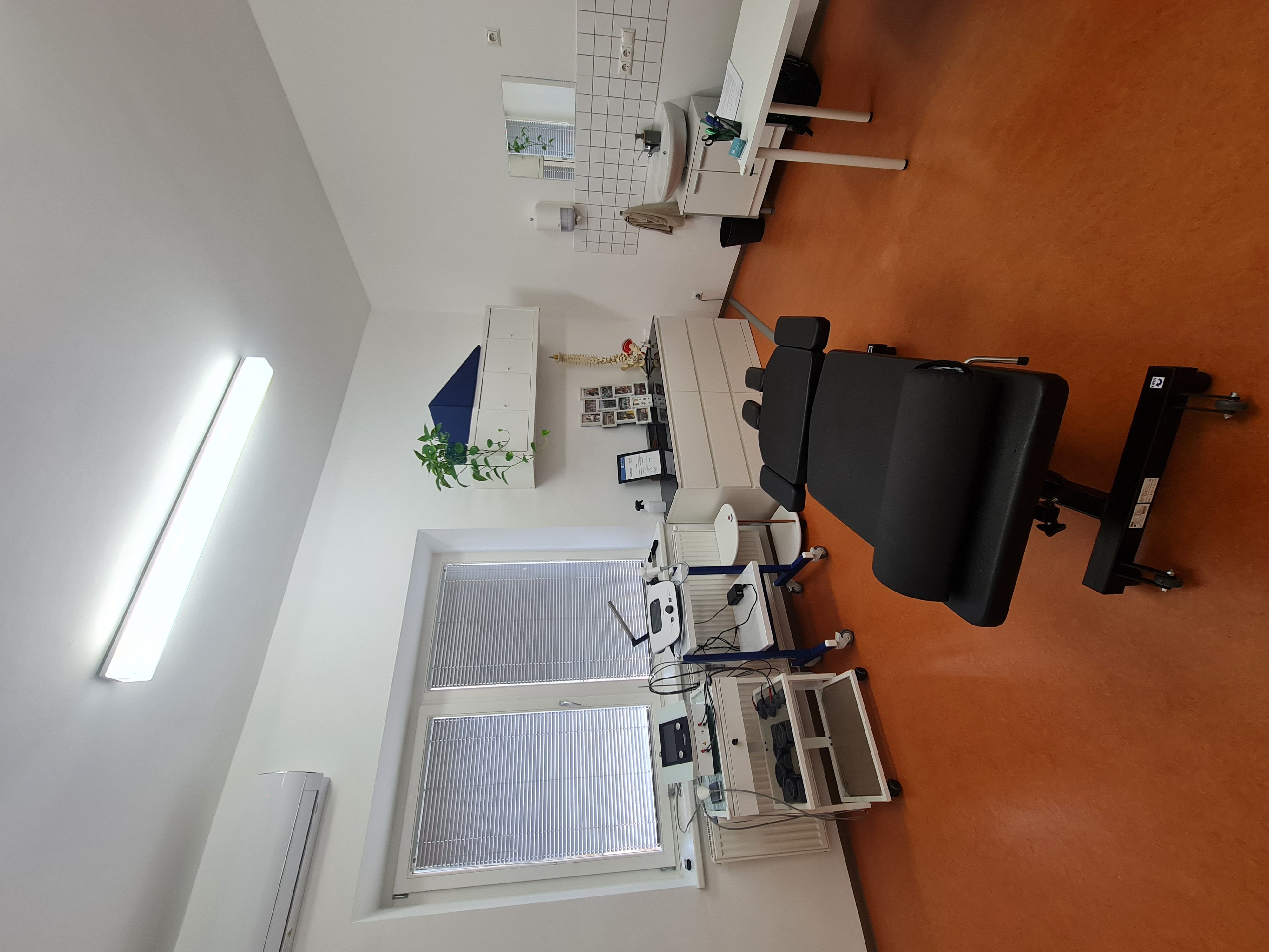 Medical examination room with specialized diagnostic equipment and a black adjustable patient chair.