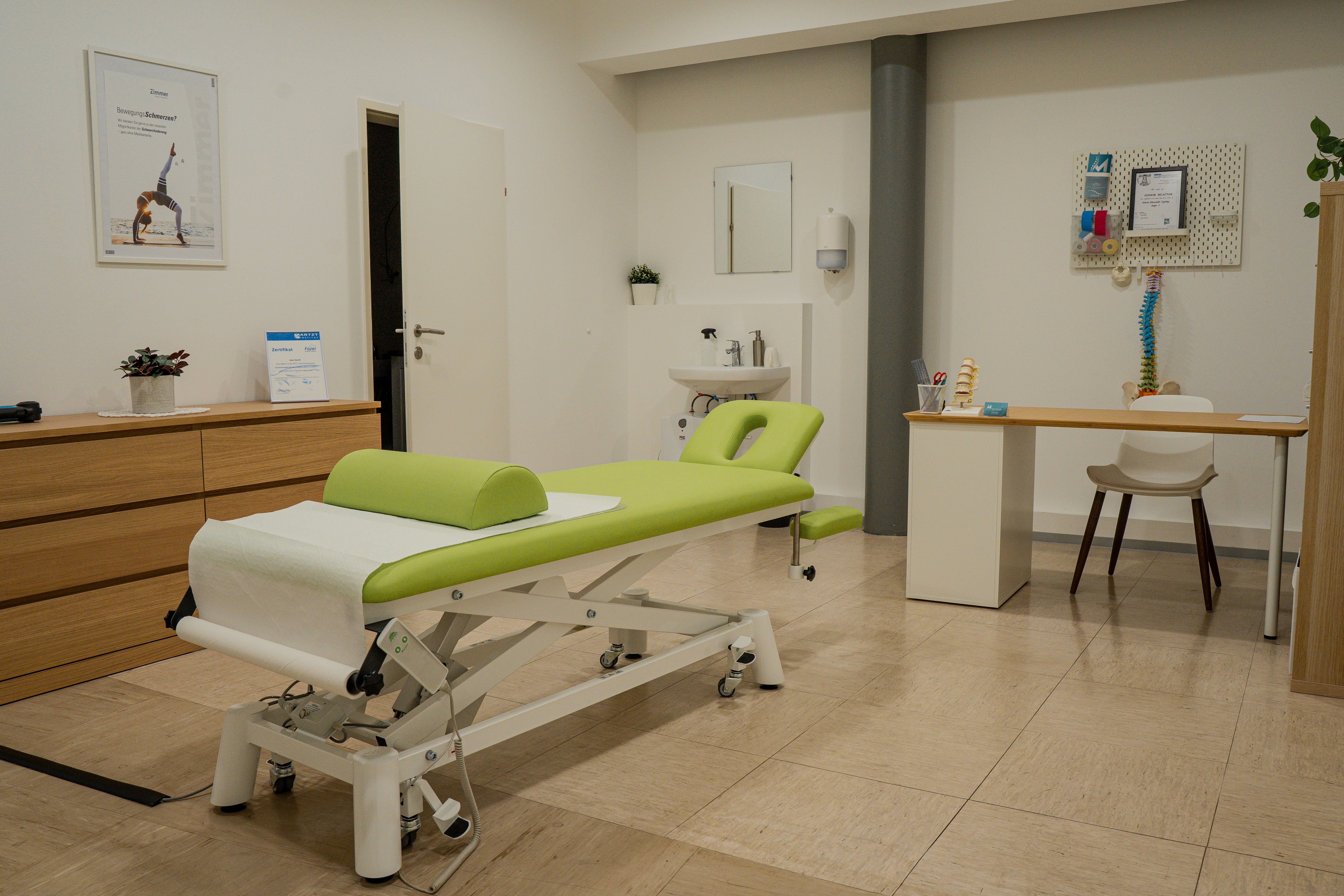 Clean, well-lit physiotherapy room featuring a green treatment table, wooden storage, and a consultation desk.