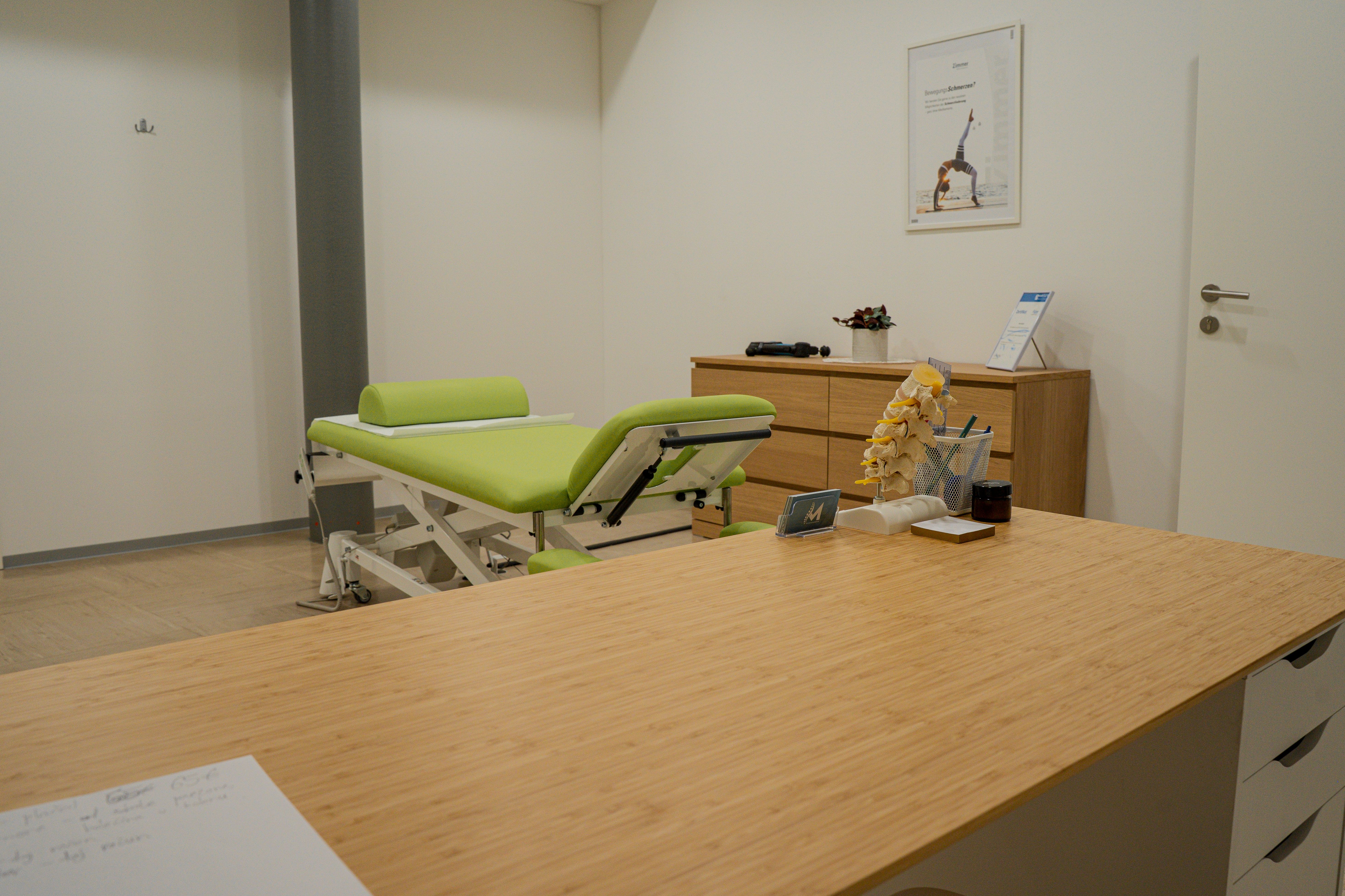 A clean, modern therapy room with a green examination table and wooden desk.