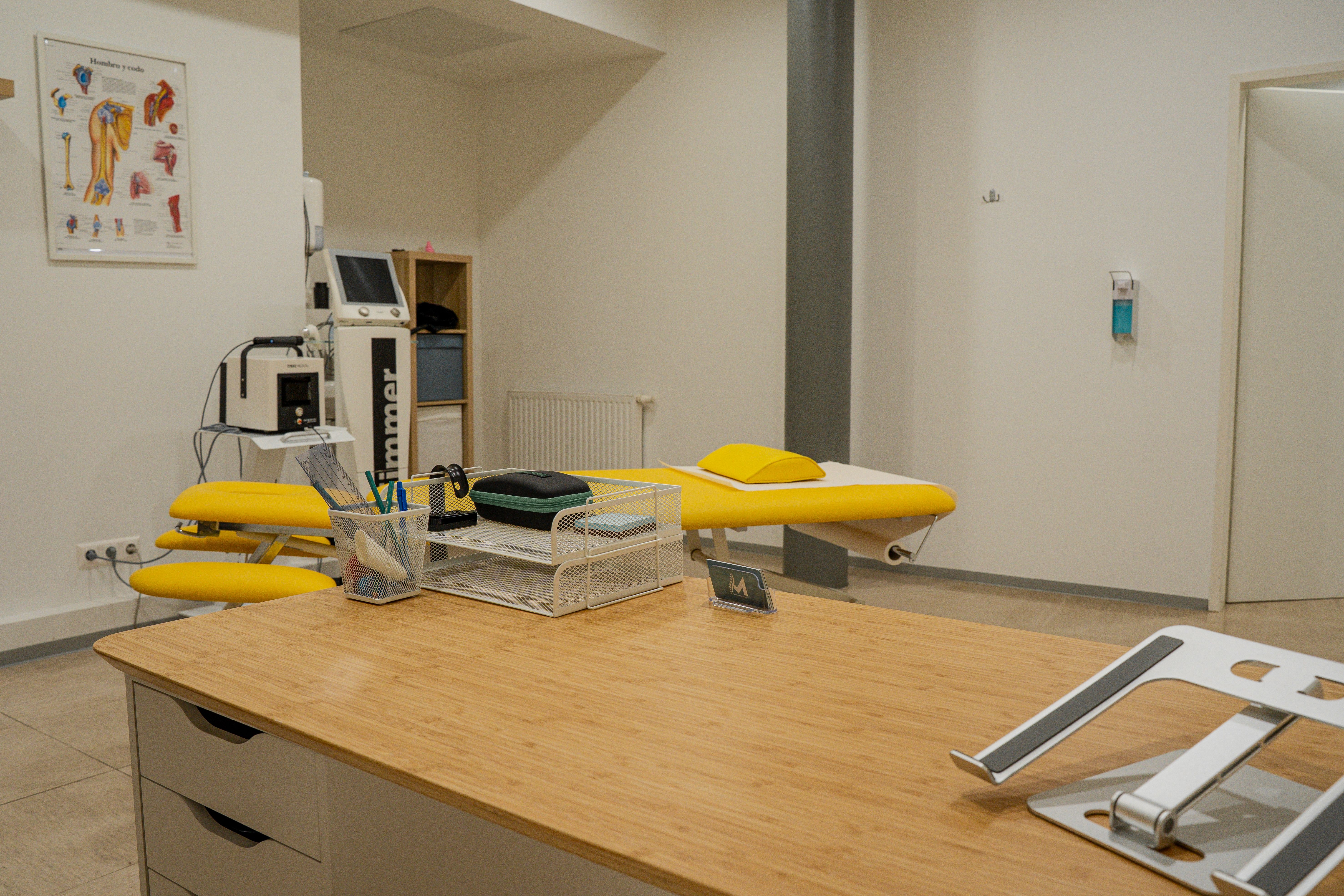 Modern medical office featuring a wooden desk, yellow examination table, and various equipment.