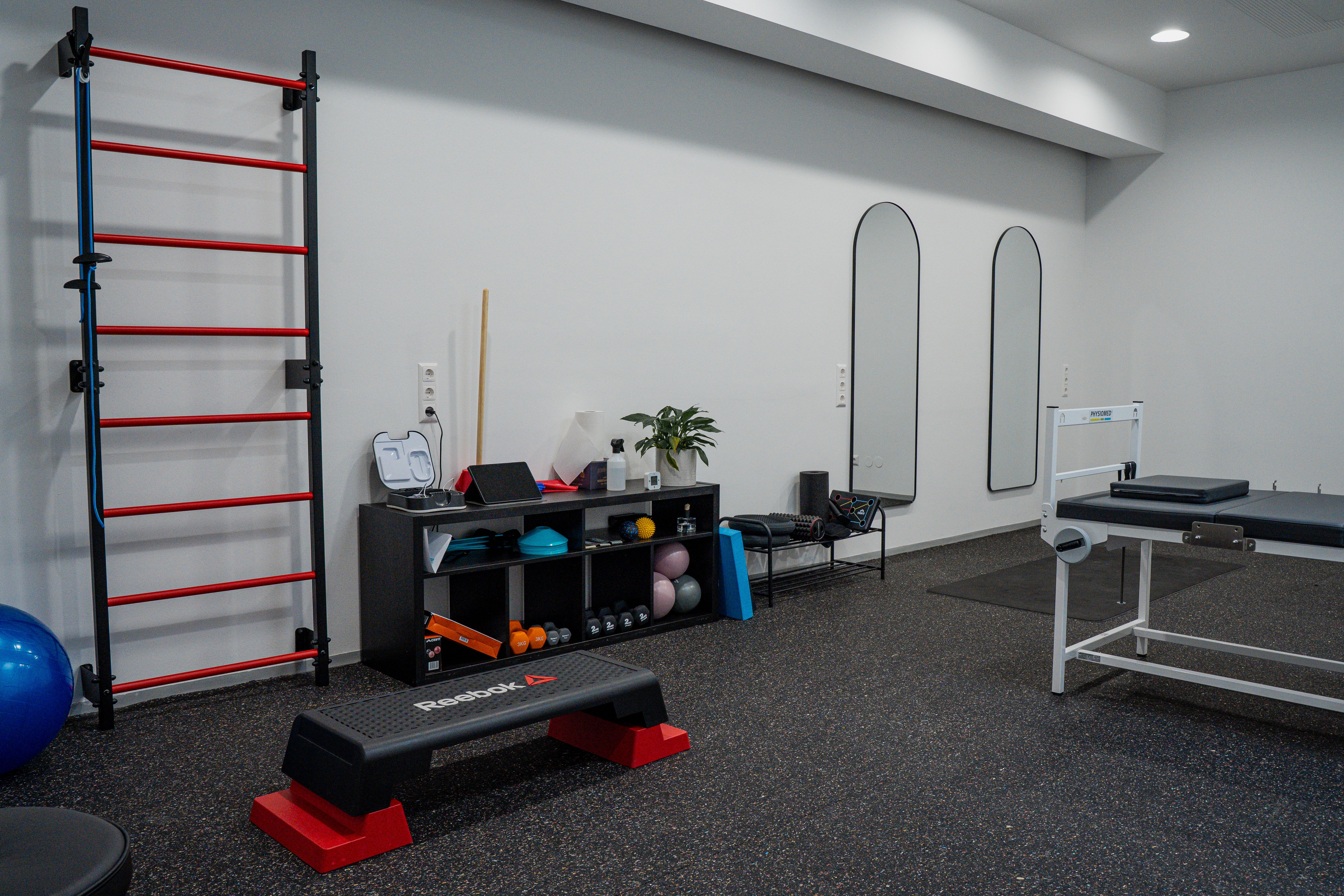 Modern physical therapy room with rehabilitation equipment, wall ladder, step platform, and mirrors.