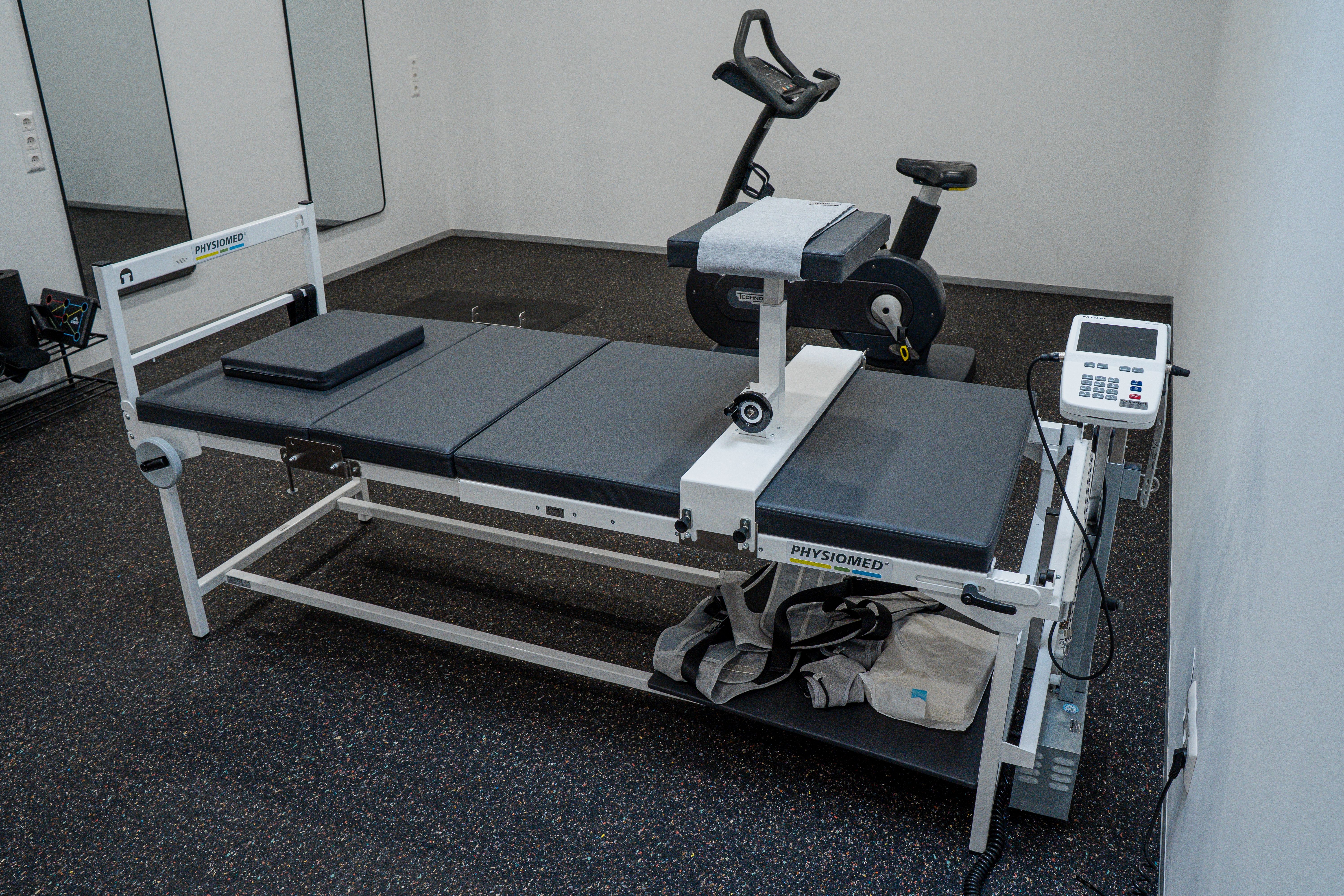 A white medical examination table with an attached exercise unit and stationary bike in a room.