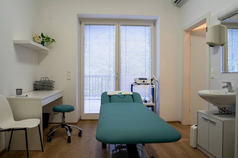Modern physical therapy room with an examination table, desk, and sink.