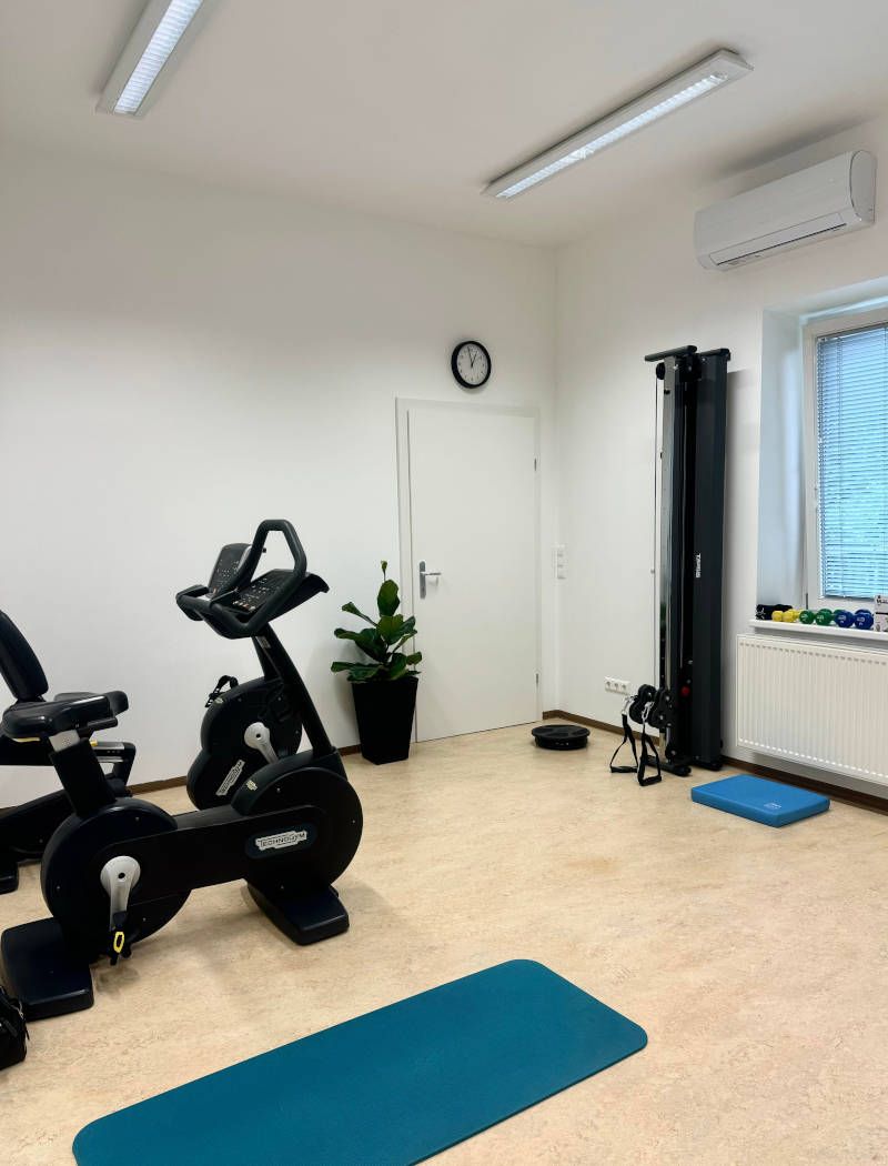 Clean home gym with a black stationary bike, blue yoga mat, and light wooden floor.
