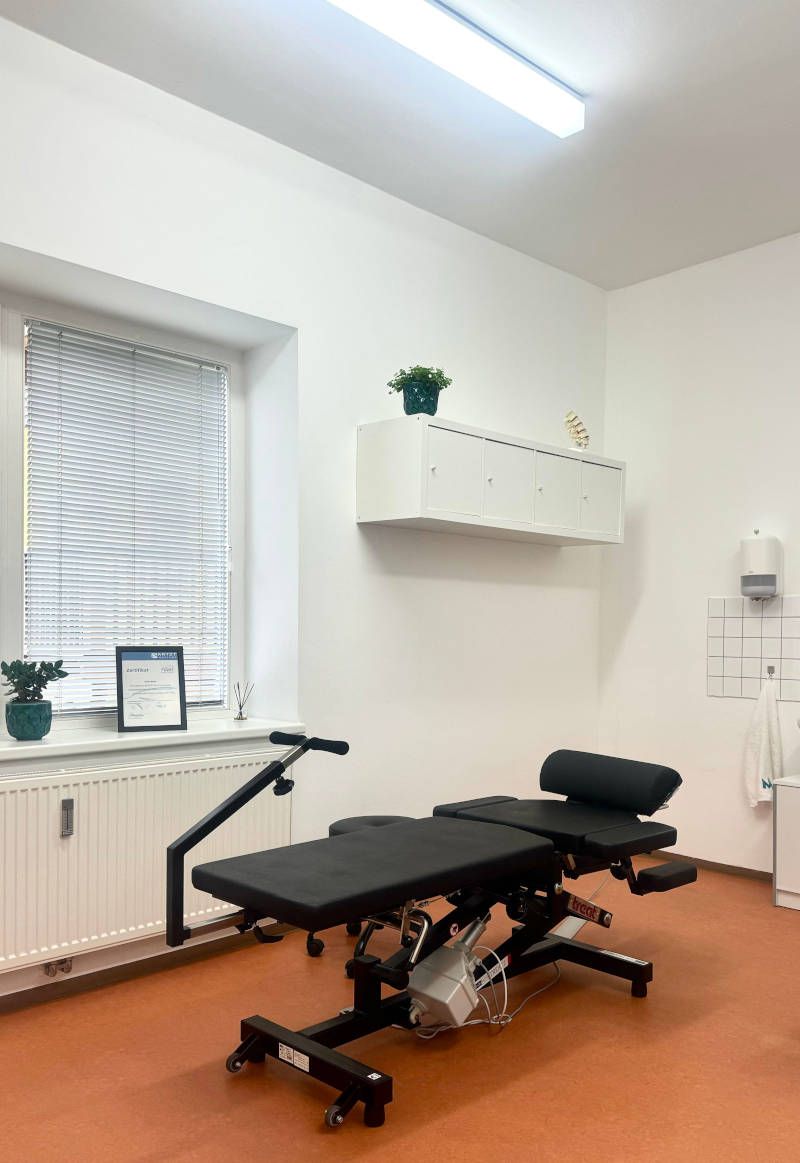 Modern medical room with a black adjustable treatment table, white walls, and orange floor.